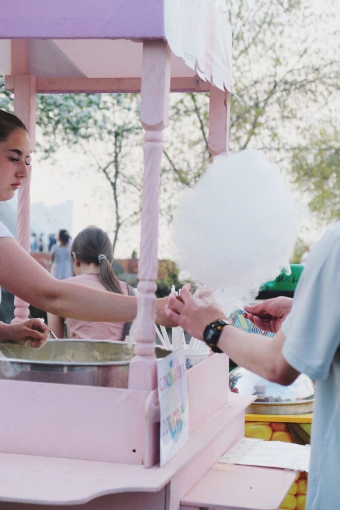 A colorful street vendor serves fluffy cotton candy to customers outdoors.