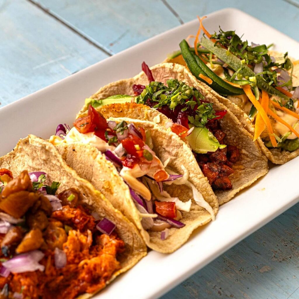 Four savory tacos with diverse fillings on a wooden table, showcasing authentic Mexican cuisine.