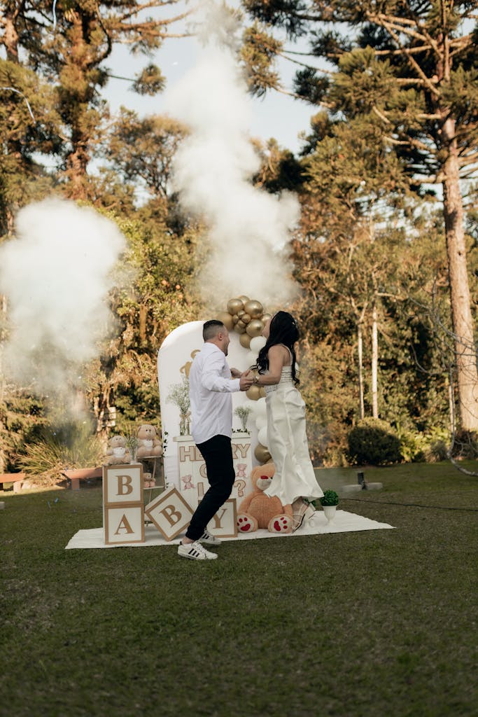 A couple enjoying an outdoor baby shower with smoke and decorations, celebrating a gender reveal.
